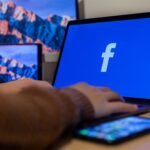 Laptop displaying Facebook at workspace with multiple devices, highlighting modern technology.
